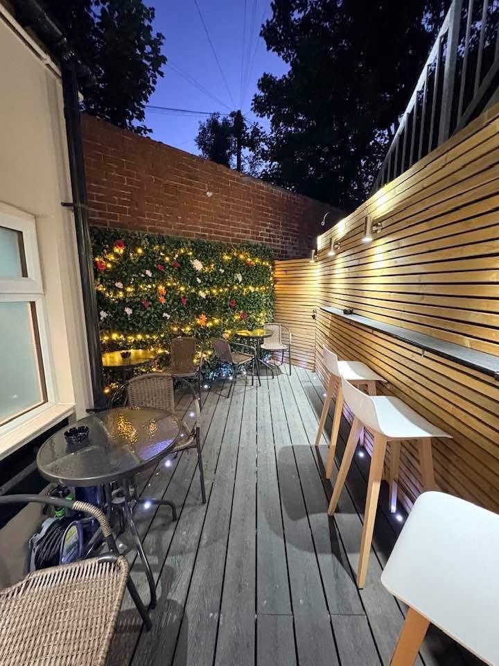 Tram Stop outdoor patio at dusk with decking, bistro seats, bar stools and a lit garden wall
